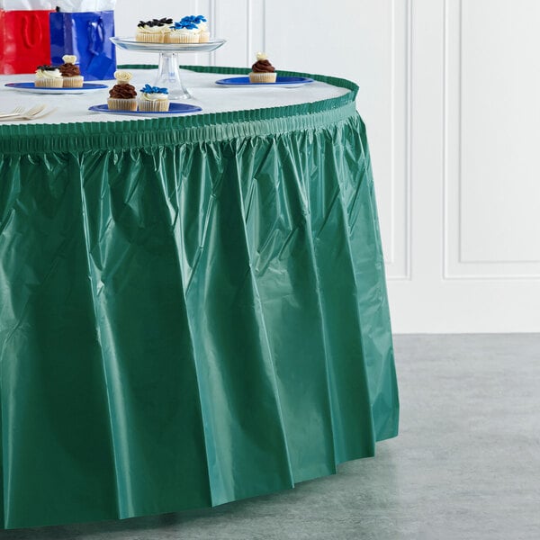 A table with a hunter green Creative Converting plastic table skirt on it.