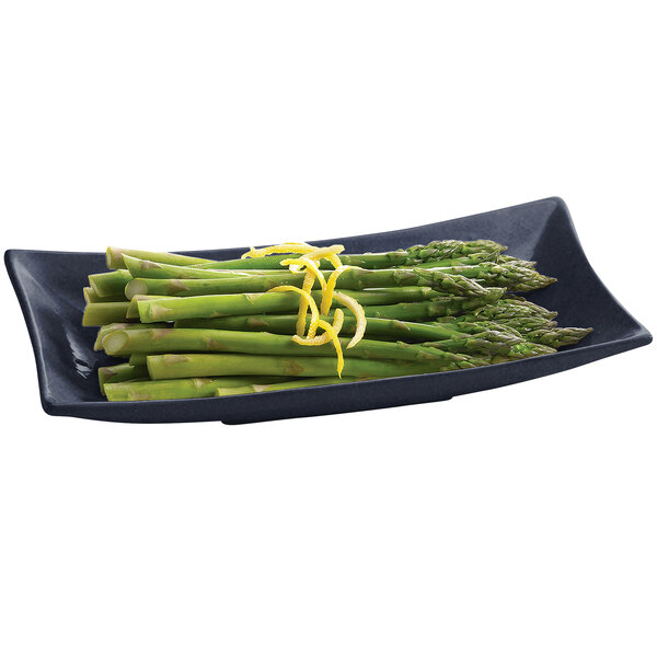 A Tablecraft midnight blue and black speckled rectangular cast aluminum platter with asparagus and lemon zest on a table.