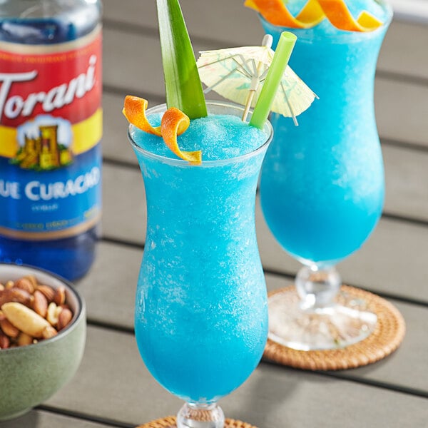 A tall glass of blue liquid with nuts and orange slices.