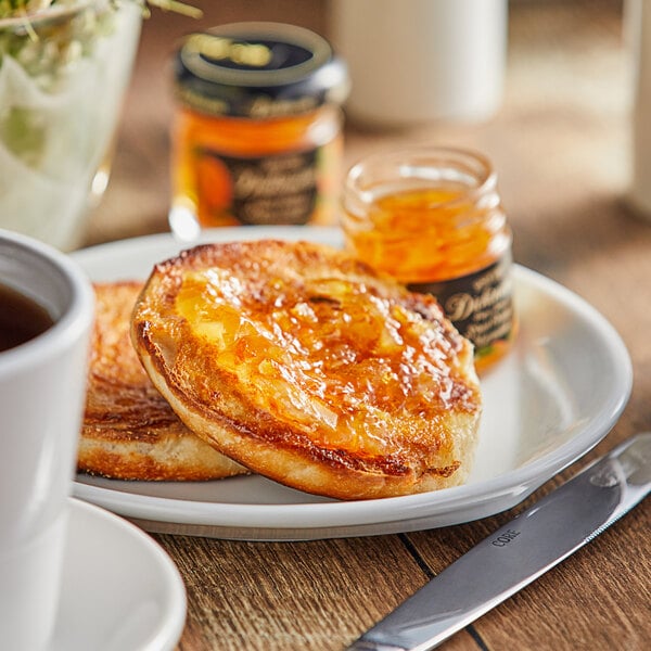 A jar of Dickinson's Pure Fancy Sweet Orange Marmalade next to a plate of food with a knife.