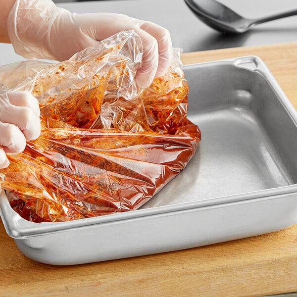 A gloved hand using a plastic bag to put red sauce in a Full Size steam table pan.