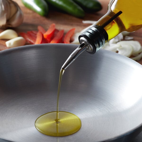 A close up of olive pomace oil pouring into a bowl of vegetables.