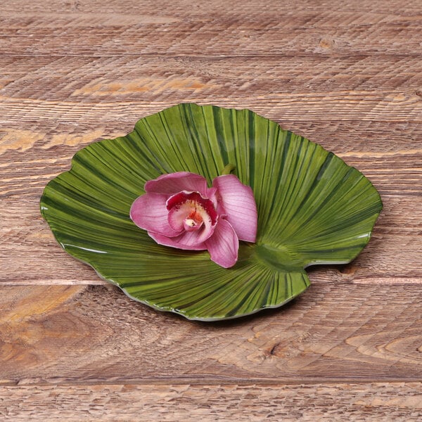 A pink flower on a green palm leaf plate.
