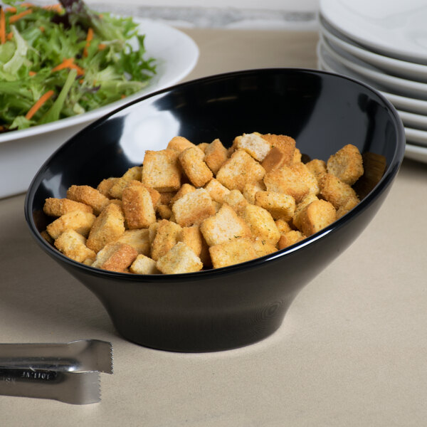 A black slanted melamine bowl filled with croutons next to a salad.