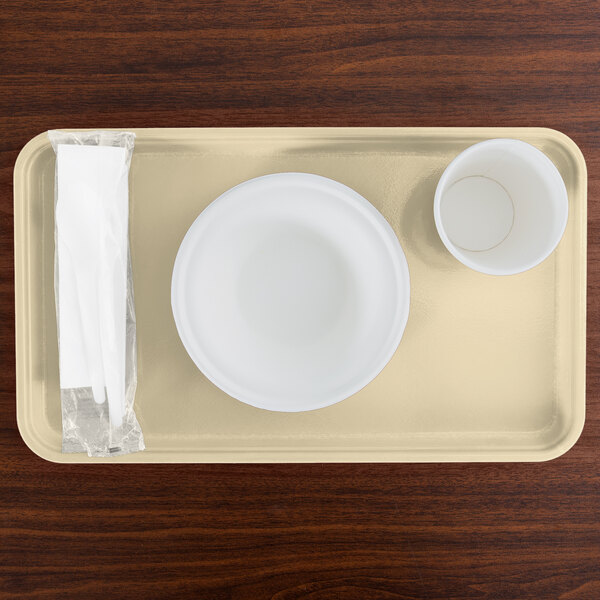 A Cambro rectangular yellow tray with a bowl and cup on a wood table.