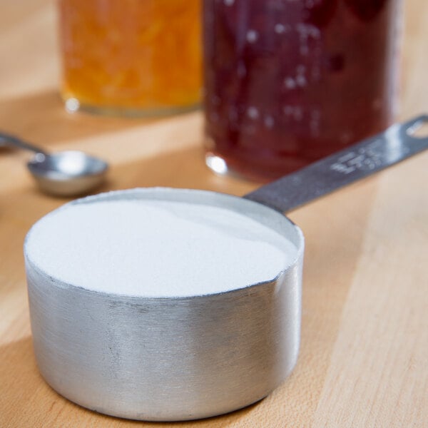 A metal container of white powder with a measuring cup and spoon on a table.
