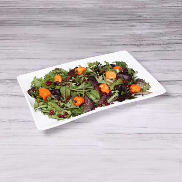 A rectangular white melamine tray with a salad of greens, orange peppers, and cranberries.