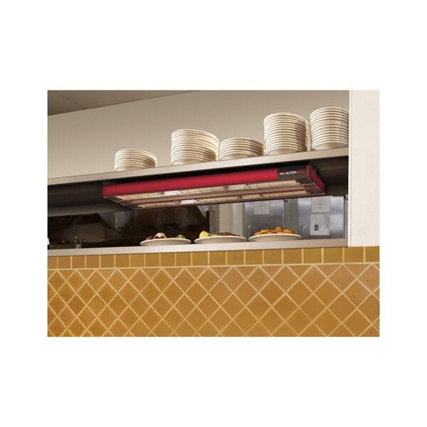 A Hatco dual infrared strip warmer above a shelf of stacked plates.