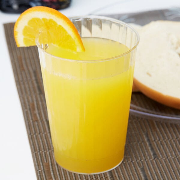 A close-up of a Fineline clear plastic tumbler filled with orange juice and a slice of orange.