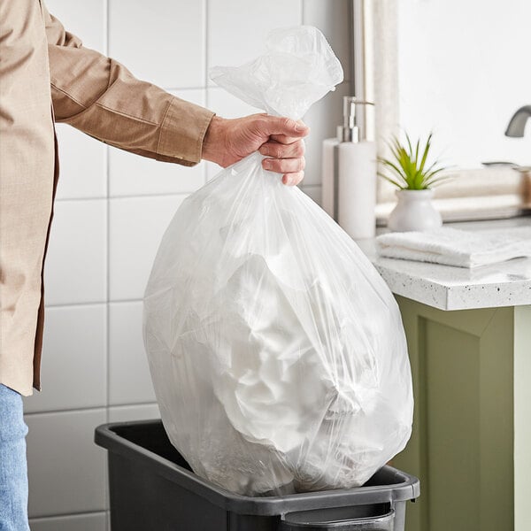 A man holding a Lavex plastic trash bag over a trash can.