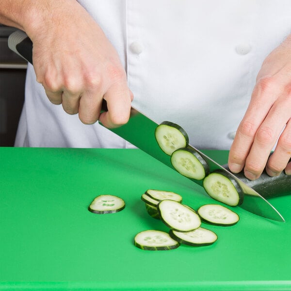 A person using a Dexter-Russell V-Lo chef knife to cut a cucumber on a cutting board.