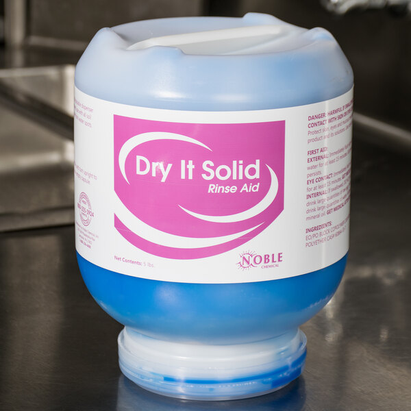 A blue container of Noble Chemical Dry It solid rinse aid on a counter.
