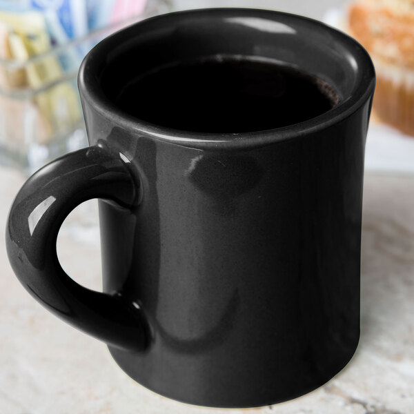 A black CAC Venice Hartford mug with a handle on a counter next to a muffin.