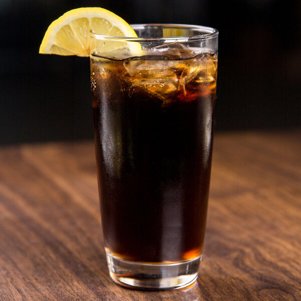 A glass of cola with ice and a lemon slice on a wooden table.