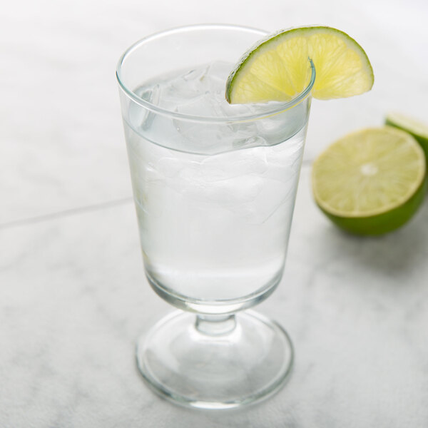A Arcoroc footed highball glass of water with ice and a slice of lime on top.