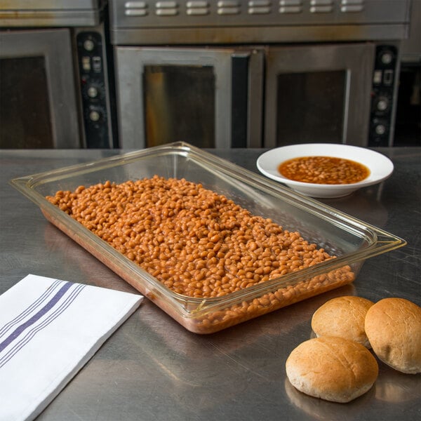 A Carlisle amber plastic food pan with beans and bread on a table.
