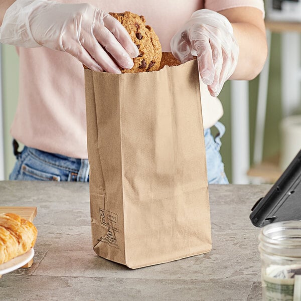 A gloved hand putting a cookie in a Duro brown paper bag.