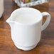 An Arcoroc white porcelain creamer on a table with milk in it.