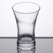 An Arcoroc clear glass shot glass with a curved rim on a table.