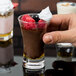 A person holding an Arcoroc shot glass of chocolate pudding with raspberries.