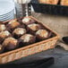 A rectangular honey plastic basket filled with muffins on a table.