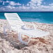 A pack of white Grosfillex Bahia chaise lounges on a beach.