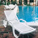 A group of white Grosfillex Bahia resin chaise lounges next to a pool.