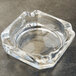 A clear glass Libbey square ashtray on a grey surface.