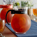 A GET Tahiti clear plastic pitcher with black handle filled with orange liquid.