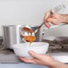 A hand using a Vollrath stainless steel ladle to pour soup into a bowl.