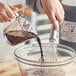 A person pouring brown liquid from a 1 gallon container into a bowl using a whisk.