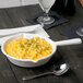 A white Tablecraft cast aluminum fry pan filled with macaroni and cheese on a table with a glass of wine.