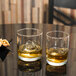 Two Libbey Room Tumblers with whiskey and ice sit on a table with nuts.
