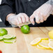 A person in gloves using a Victorinox chef knife to cut a lime.