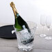 A bottle of champagne in a Thunder Group wine bucket of ice with a glass of wine on a table.
