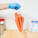 A person wearing blue gloves holding an Inteplast Group plastic food bag full of carrots.