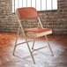 A beige National Public Seating metal folding chair with a honey brown vinyl padded seat.