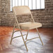 A beige National Public Seating metal folding chair with French beige vinyl padding.