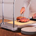 A chef using a knife to cut meat on an Alto-Shaam carving station tray.