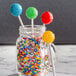 A glass jar filled with colorful lollipops on blue and white paper lollipop sticks.