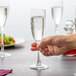 A close up of a hand holding an Arcoroc Rutherford champagne flute filled with champagne.