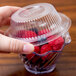 A person holding a plastic container with a clear lid filled with raspberries.
