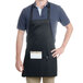 A man wearing a black Chef Revival bib apron with a pocket in a professional kitchen.