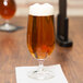 A Spiegelau Vino Grande stemmed Pilsner glass full of beer on a table with a napkin.