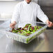 A chef holding a Rubbermaid clear plastic colander / drain tray of salad.