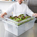 A chef holding a Rubbermaid clear colander drain tray filled with salad greens.