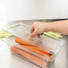 A hand putting carrots into a clear Rubbermaid food container with a lid.