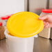 A hand holding a yellow lid over a Rubbermaid plastic container.