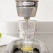 A Nemco Easy Citrus Juicer cone attached to a glass of juice being poured into a metal pipe.