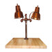 A Hanson Heat Lamps smoked copper carving station with maple block and gravy lane with dual copper lamps over a wooden surface.